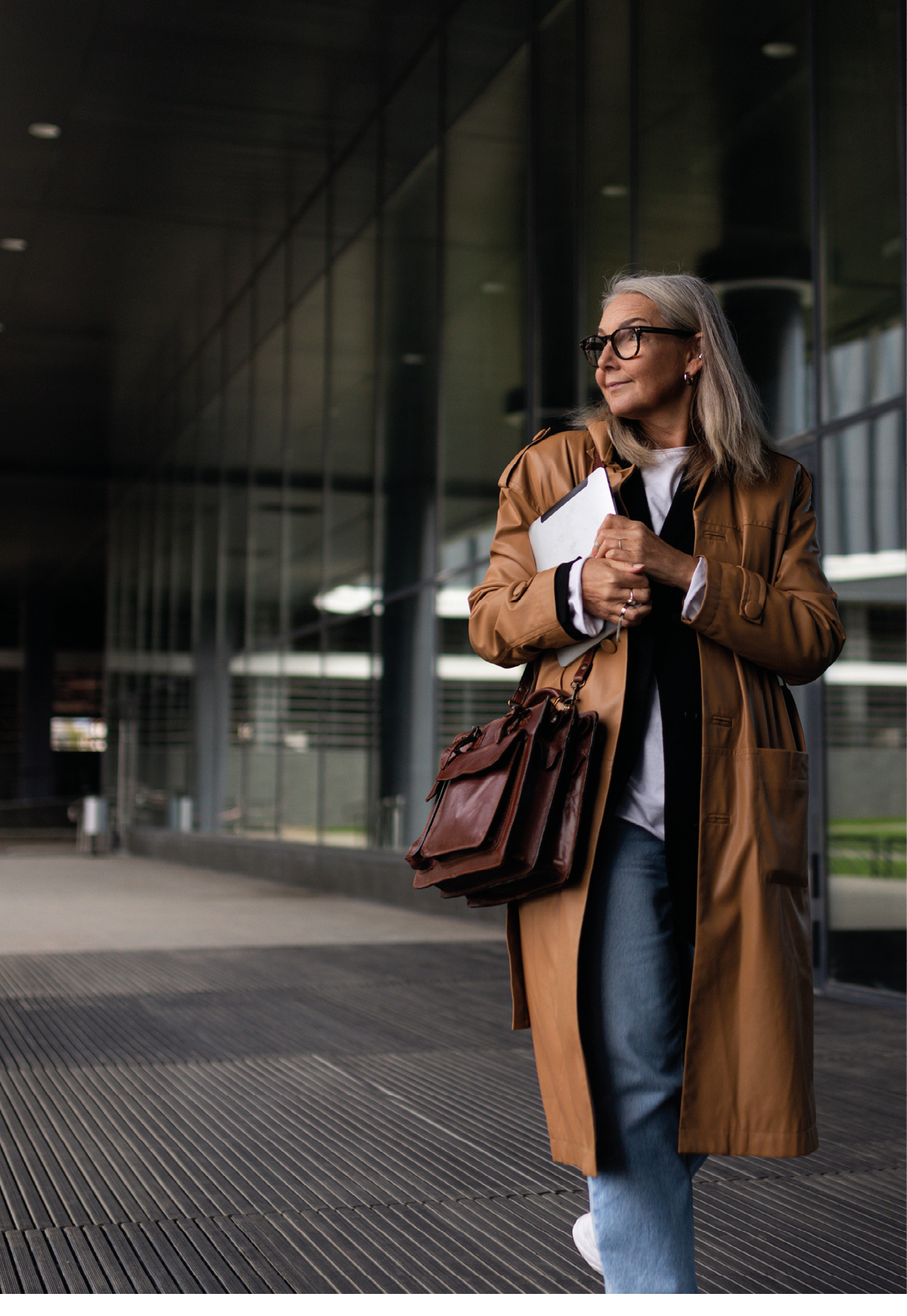 a female research analyst at a bank or brokerage firm is walking along the road to the office with a laptop in her hands against the backdrop of a business center..